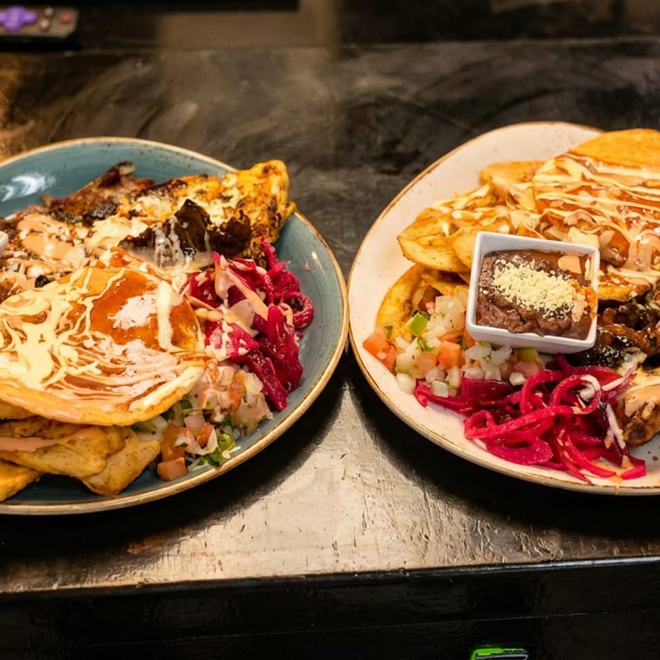 Two hearty platters featuring grilled meat, fried plantains, pickled cabbage, beans, and creamy sauce.